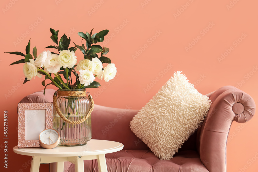 Vase with ranunculus flowers, frame and clock on table in living room