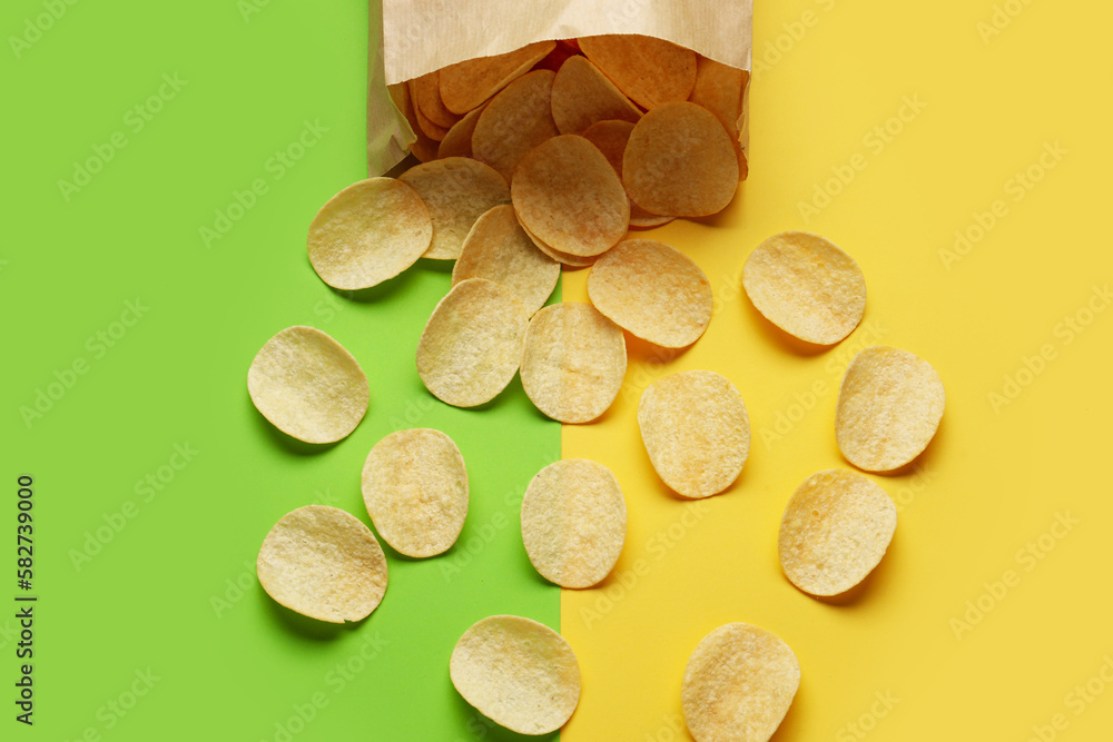 Overturned paper bag with delicious potato chips on green and yellow background