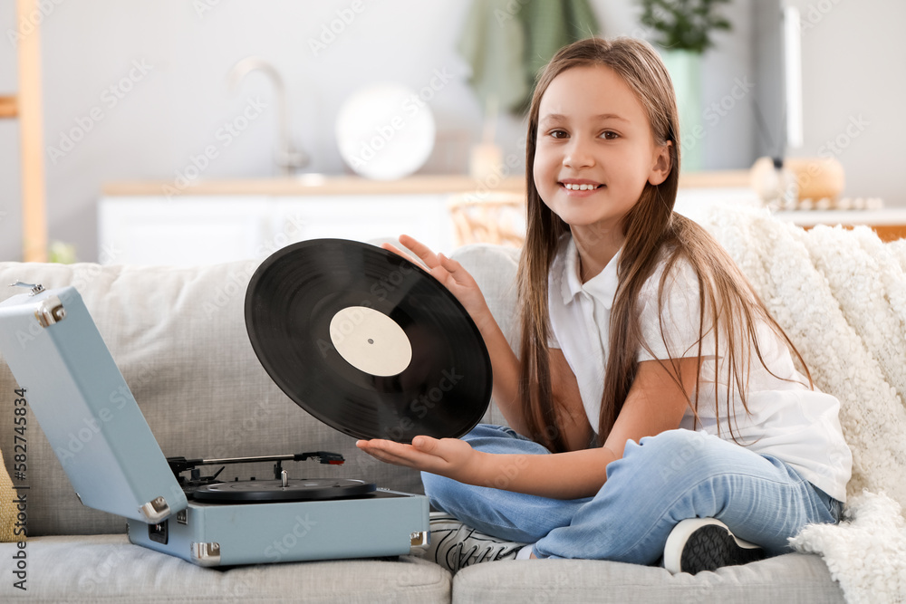 Little girl with vinyl disc and record player sitting on sofa at home