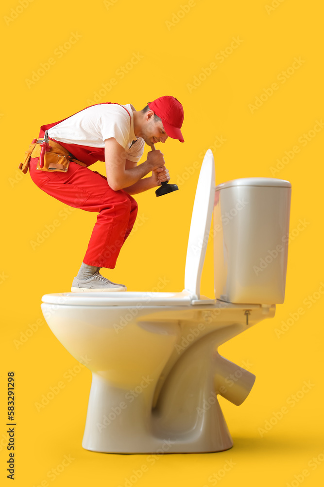 Young plumber with plunger and toilet bowl on yellow background