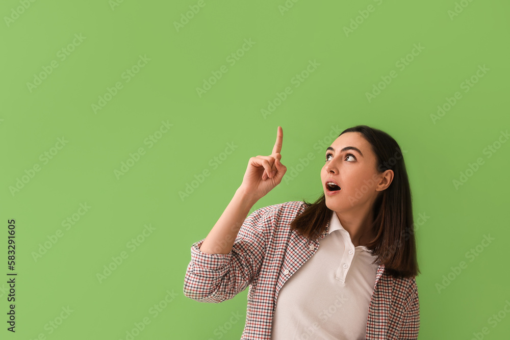 Shocked young woman pointing at something on green background