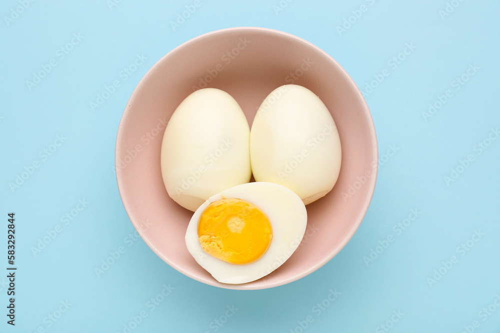 Bowl with delicious boiled eggs on blue background