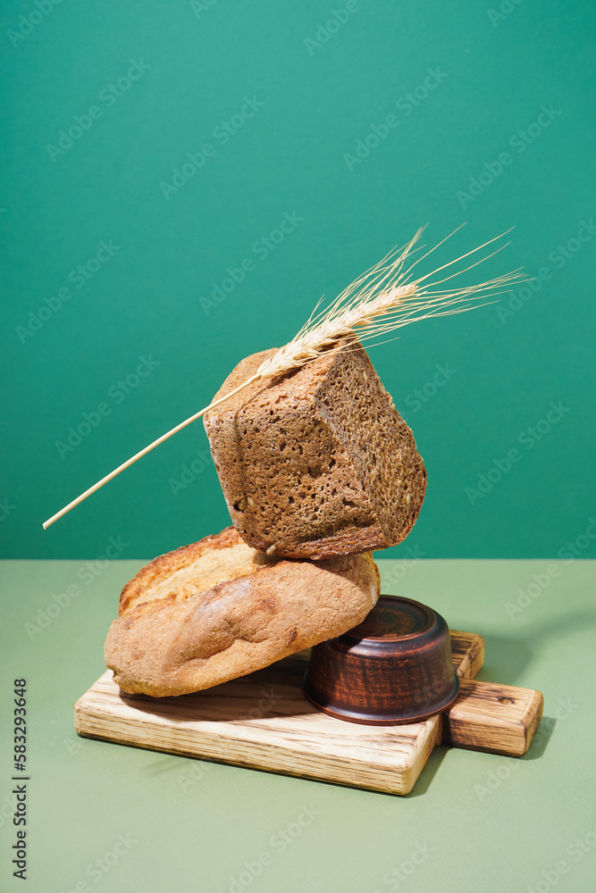 Board with loaves of fresh bread and wheat ear on green table