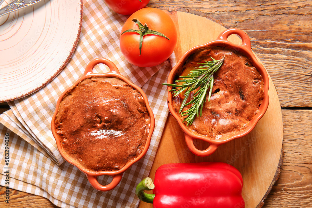 Board with delicious meat pies in baking forms and vegetables on wooden table