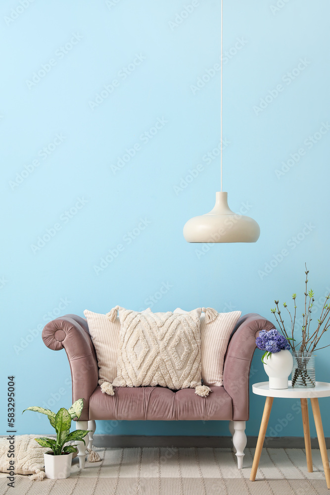 Cozy sofa with cushions, table and different plants near blue wall