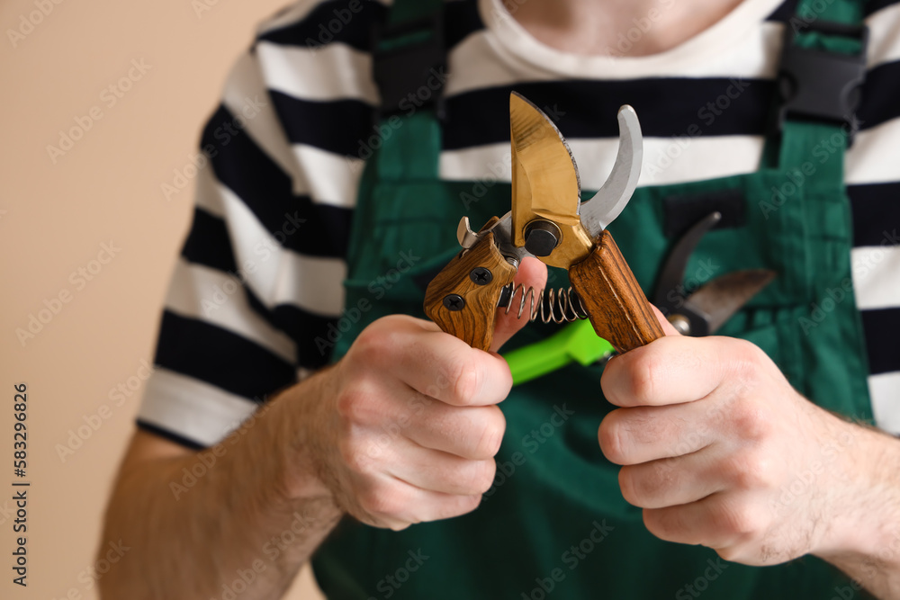 Male gardener with secateurs on beige background, closeup