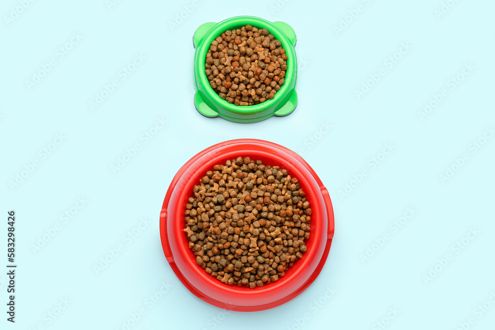 Bowls of dry pet food on color background