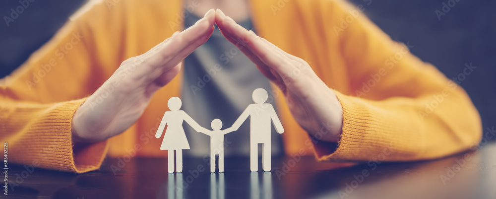 Woman holding her hands in the form of a roof over the figurines of a family.