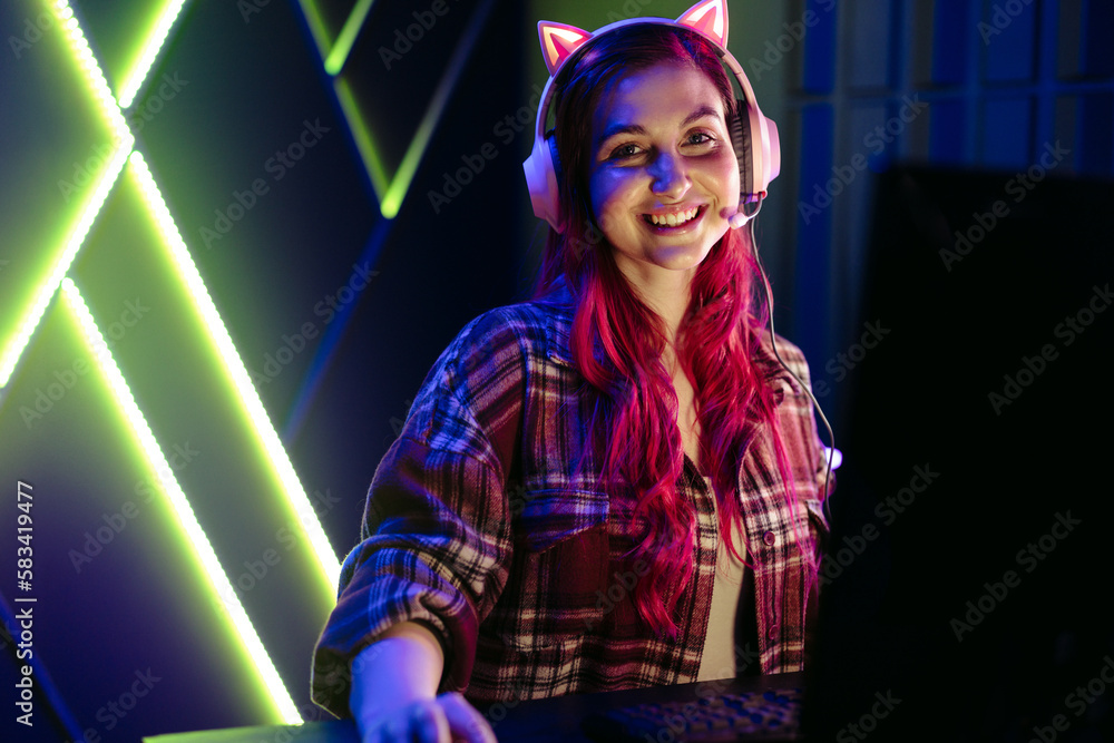 Portrait of a happy female gamer sitting in front of a gaming computer