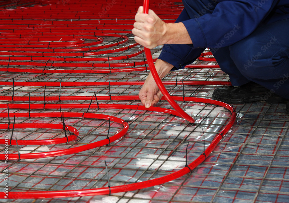 Worker is installing a red pipe for underfloor heating