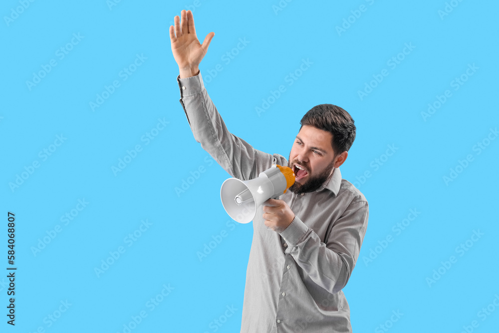 Angry young man shouting into megaphone on blue background