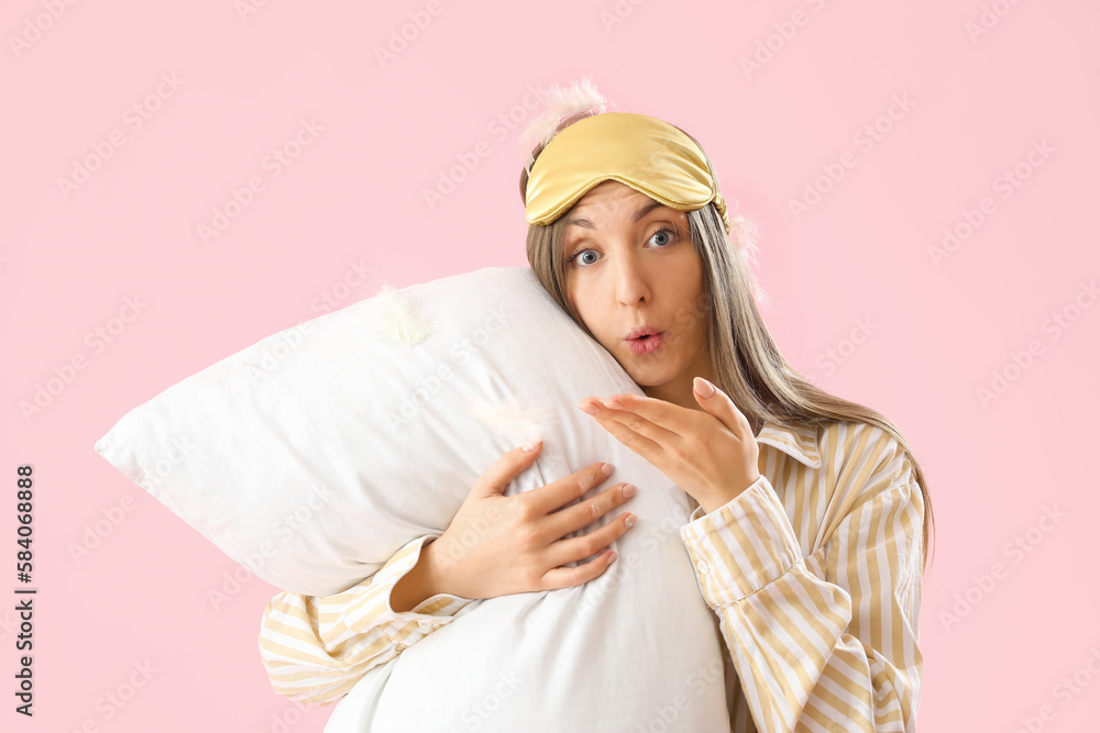 Young woman with sleeping mask, pillow and feathers on pink background