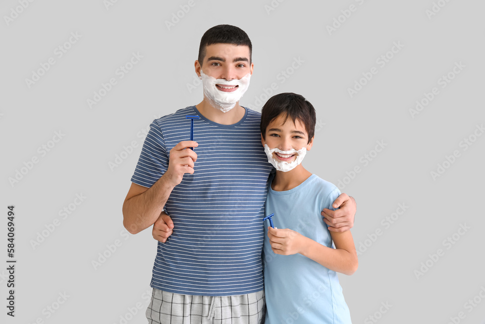 Father and his little son shaving against light background