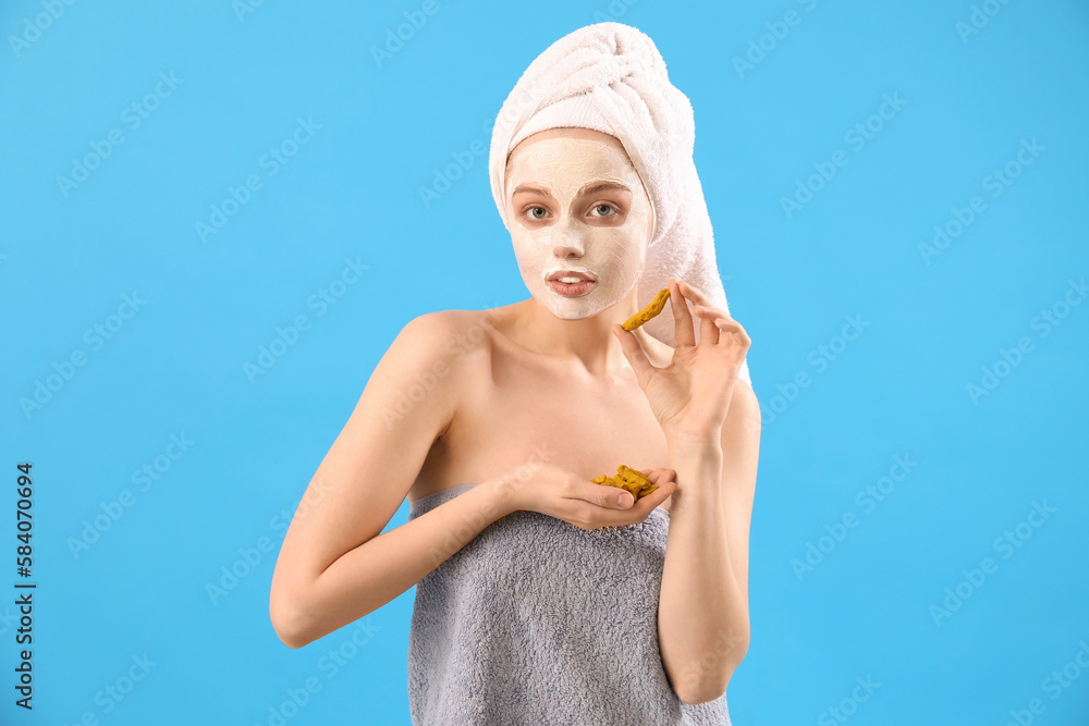 Young woman with applied turmeric mask and roots on blue background