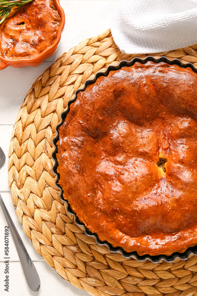 Wicker mat with delicious meat pie in baking form on white wooden table