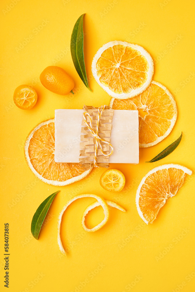 Composition with natural soap bar, dried orange slices and kumquat on yellow background