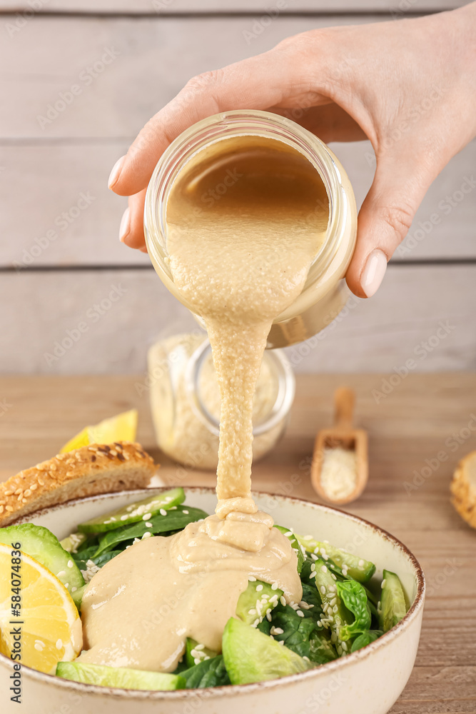 Woman adding tahini into bowl of salad on wooden table, closeup