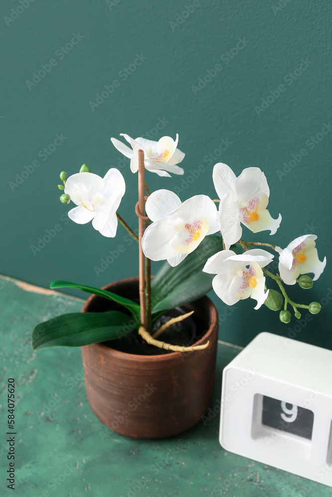 Artificial flower with clock on table near green wall