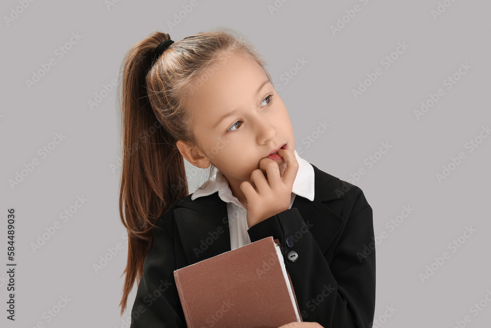 Little schoolgirl with book biting nails on grey background, closeup