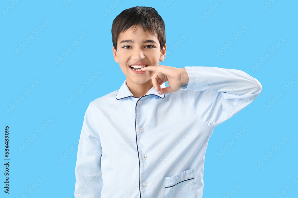 Little boy in pajamas biting nails on blue background