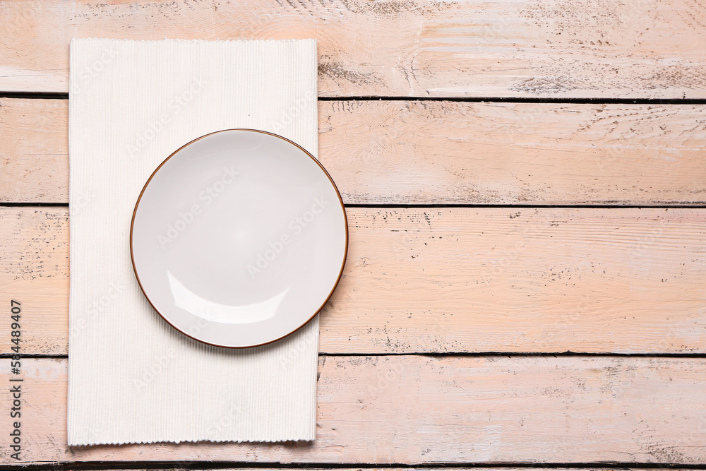 Empty plate and folded napkin on light wooden background