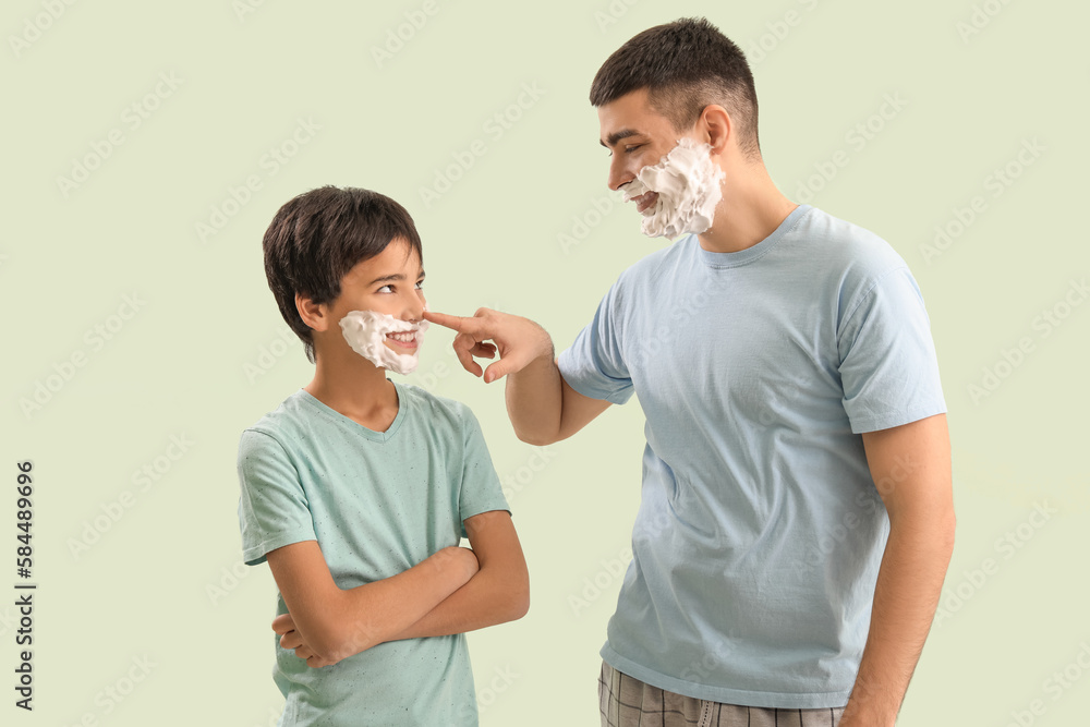 Man and his little son with shaving foam on faces against light color background