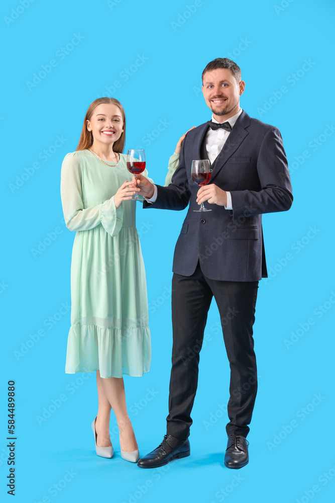 Young man in suit giving his wife glass of wine on blue background