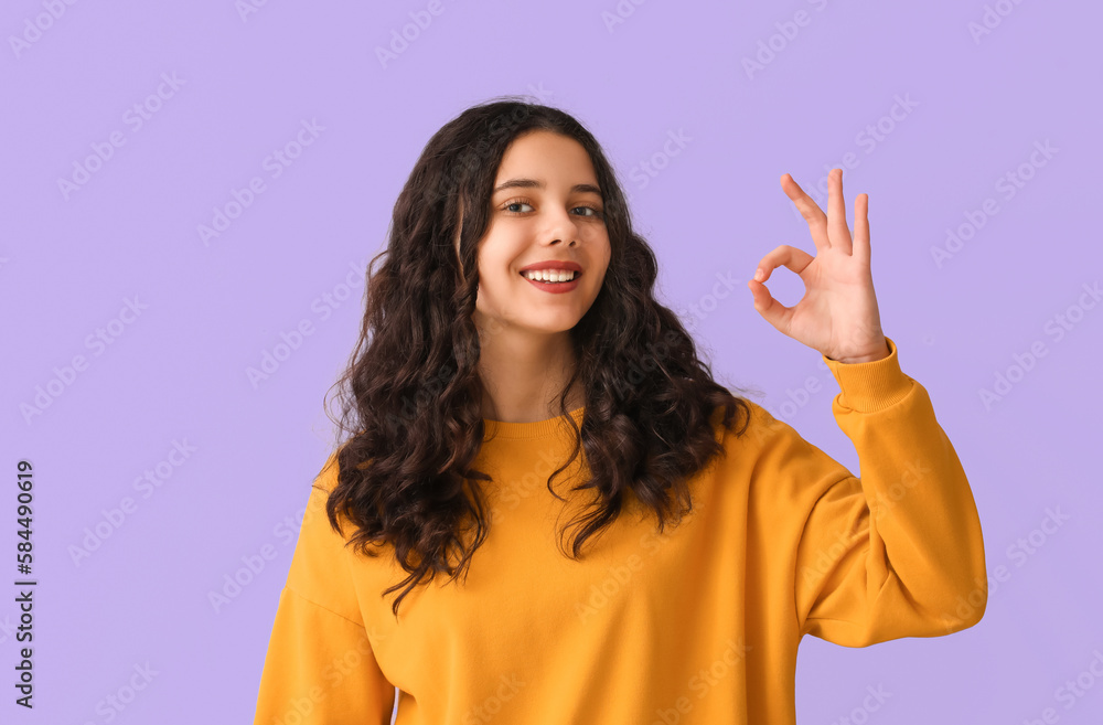 Teenage girl in yellow sweatshirt showing OK on lilac background