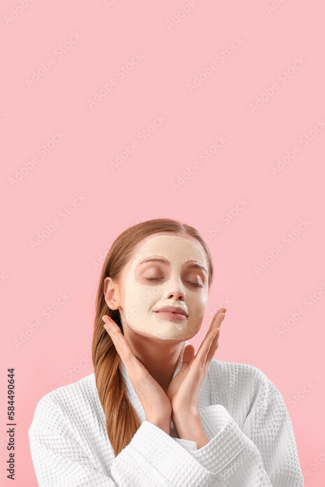 Young woman in bathrobe with applied turmeric mask on pink background