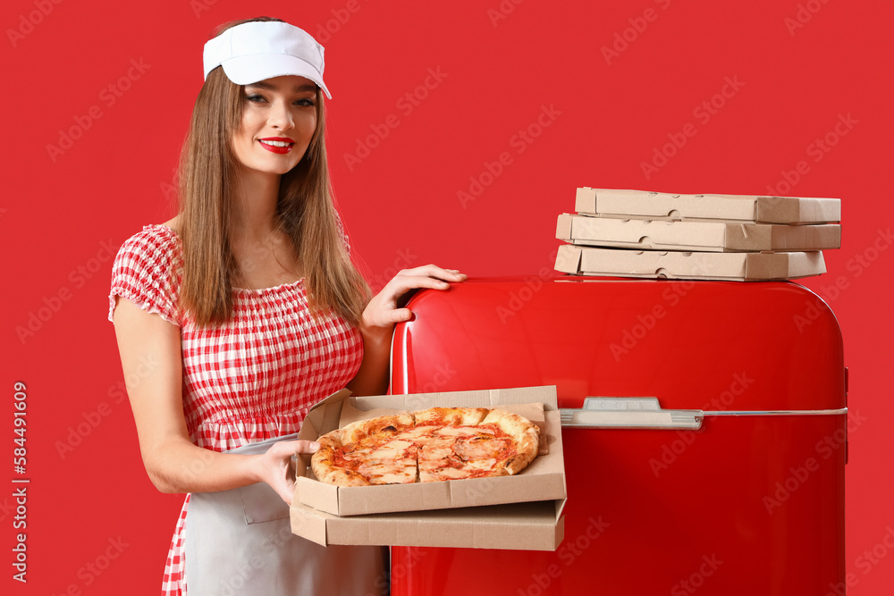 Young woman with tasty pizza and fridge on red background