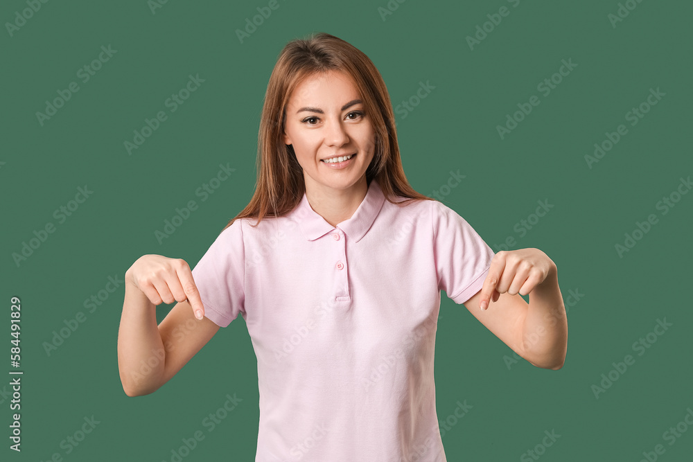 Beautiful woman in pink t-shirt pointing at something on green background