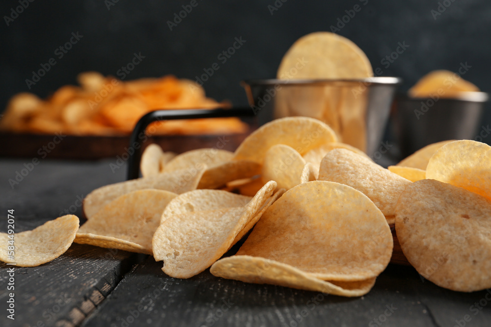 Delicious potato chips on black wooden table