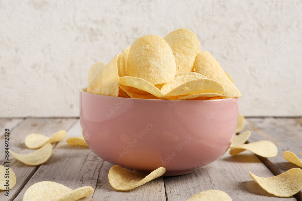 Bowl with delicious potato chips on wooden table against grey background