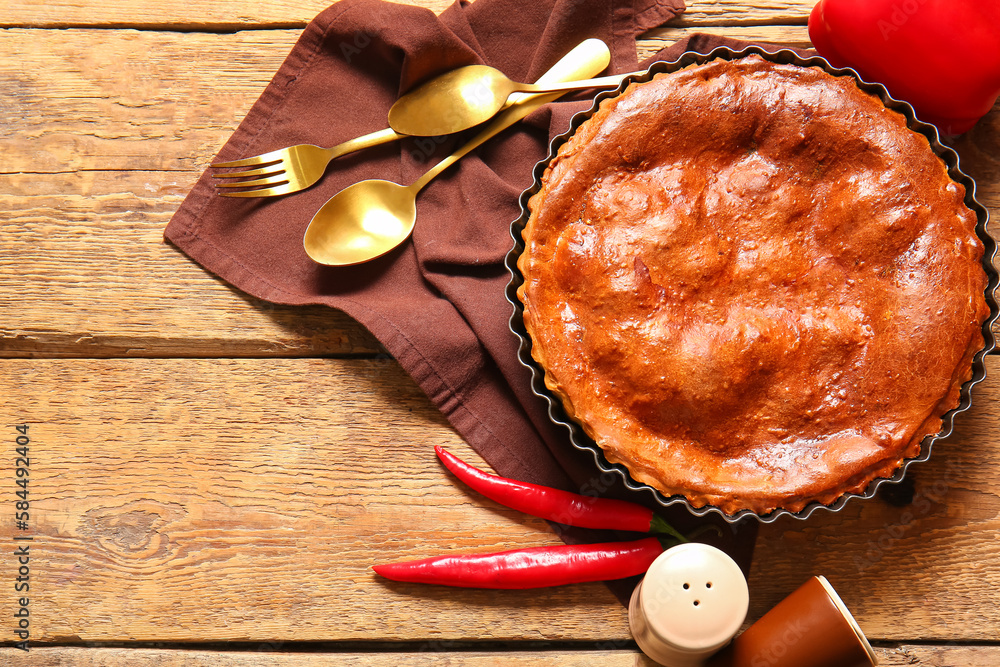 Composition with delicious meat pie in baking form and peppers on wooden table