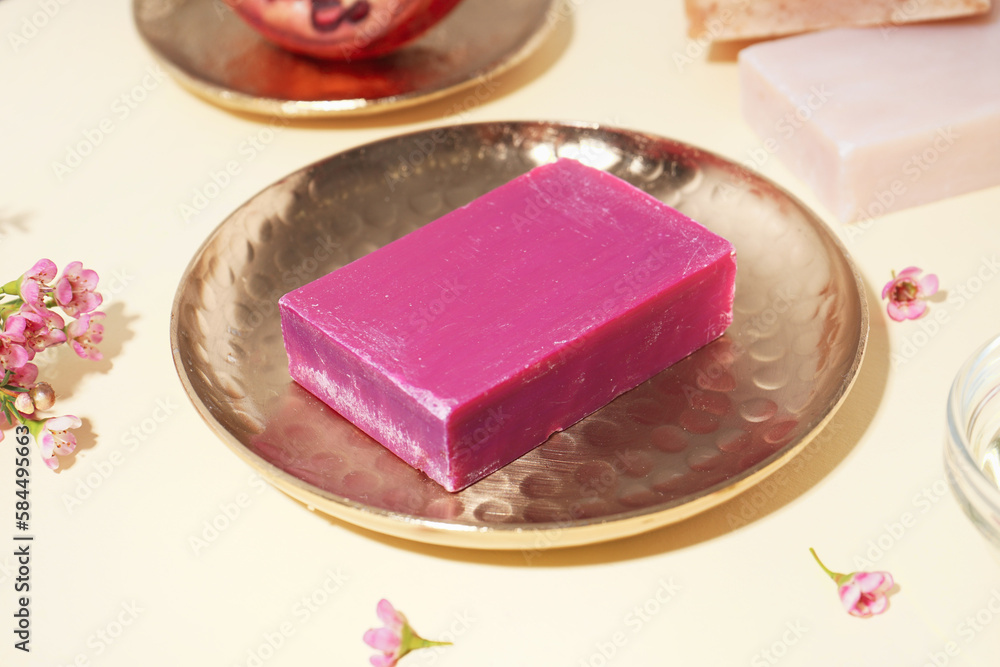 Golden plate with natural soap bar and flowers on color background