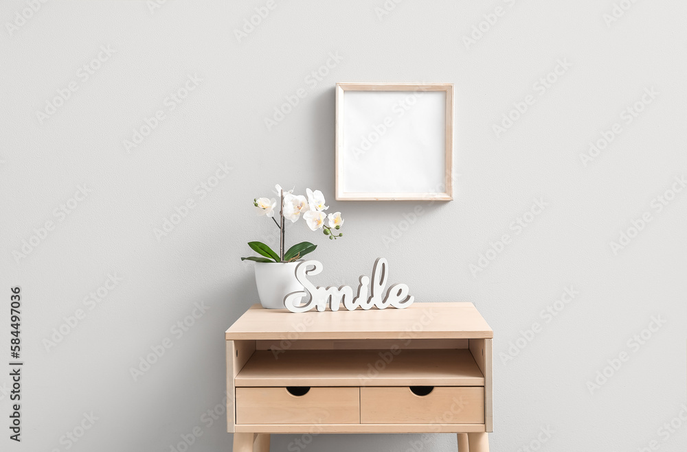 Artificial flower with decor on table near light wall