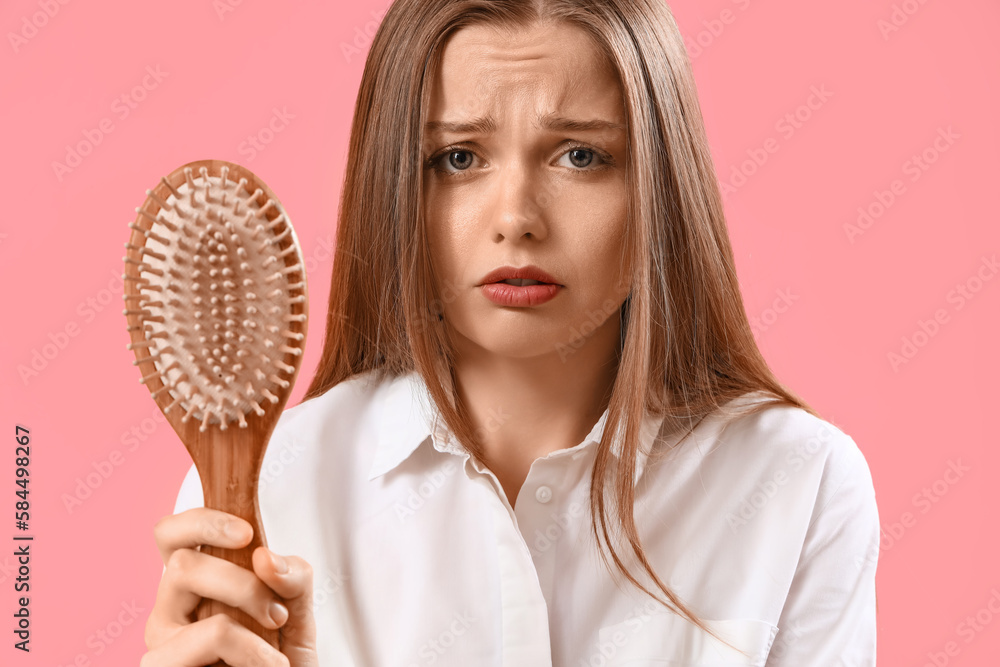 Worried young woman with hair loss problem and brush on pink background