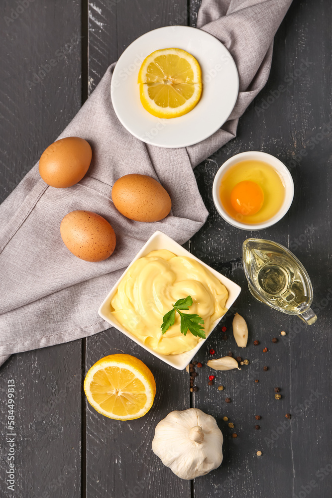 Bowl with tasty mayonnaise sauce and ingredients on dark wooden table