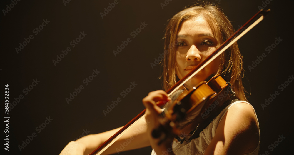 Experienced asian female violin player having a solo during the concert, spotted by light on black b