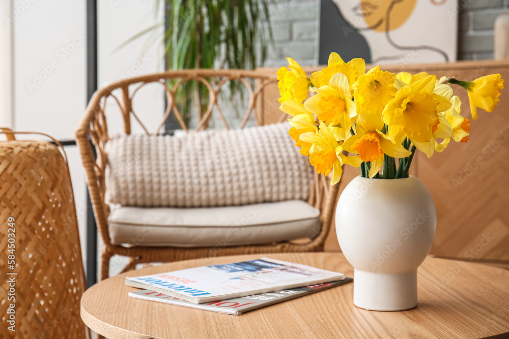 Vase with beautiful narcissus flowers and magazines on coffee table in living room