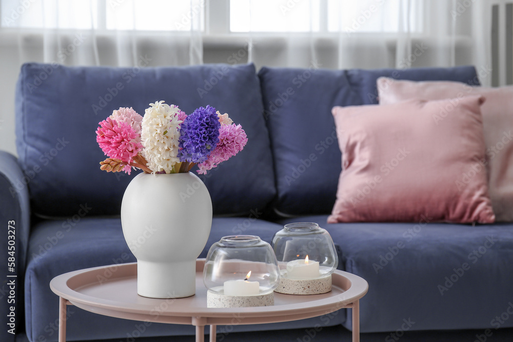 Vase with beautiful hyacinth flowers and burning candles on coffee table in living room