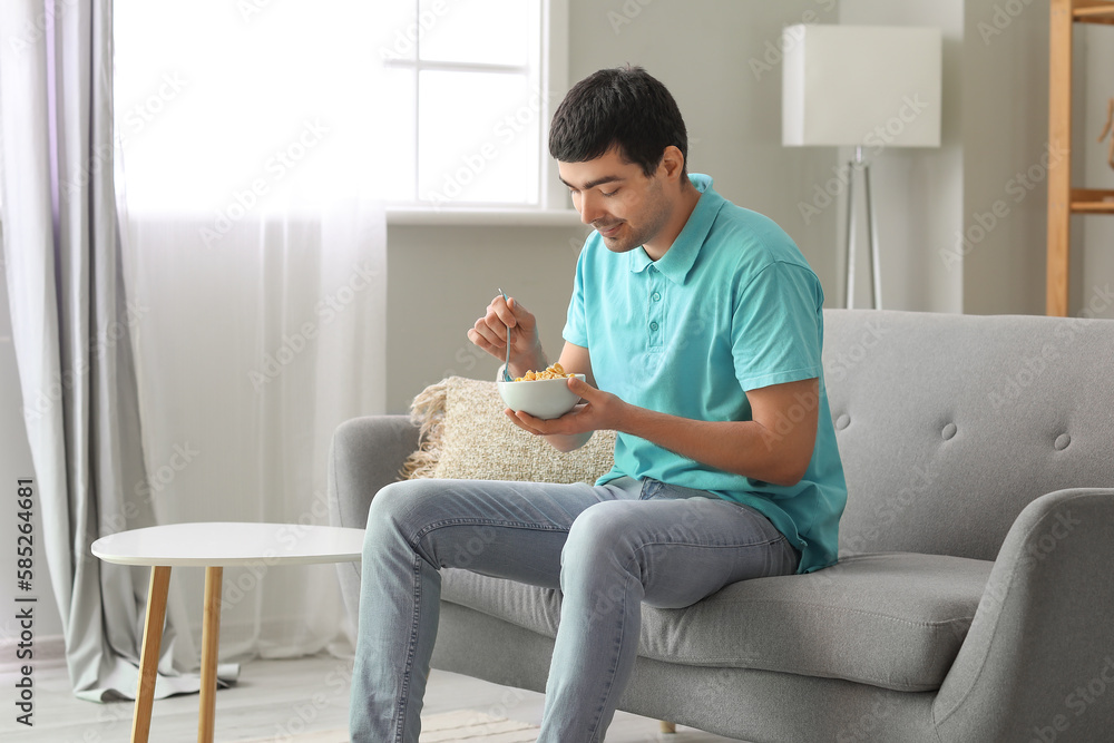 Young man eating cornflakes with spoon at home