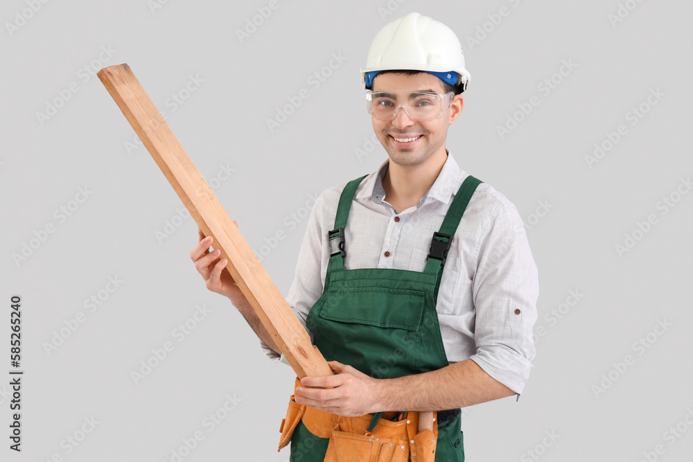 Young carpenter with wooden plank on grey background