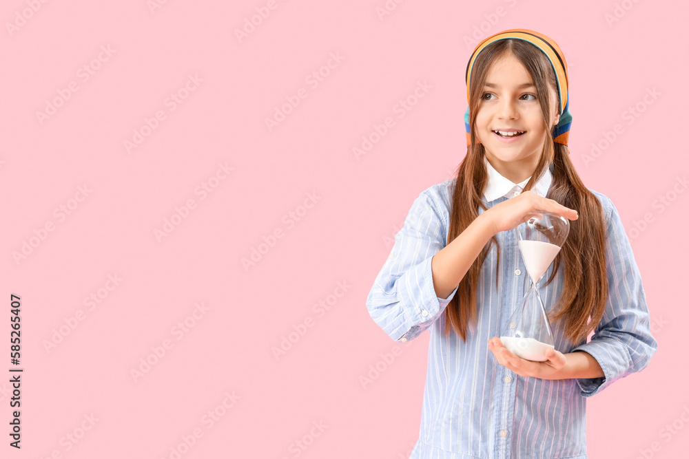 Little girl with hourglass on pink background