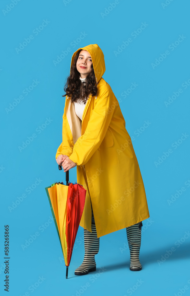 Teenage girl in raincoat with umbrella on blue background