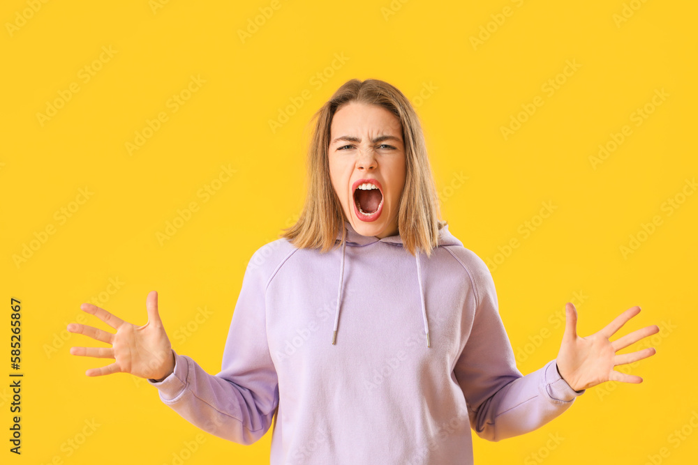 Angry young woman in lilac hoodie on yellow background