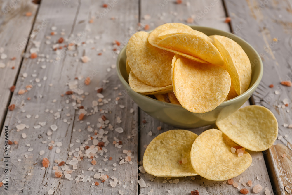 Bowl with delicious potato chips and sea salt on grey wooden table, closeup