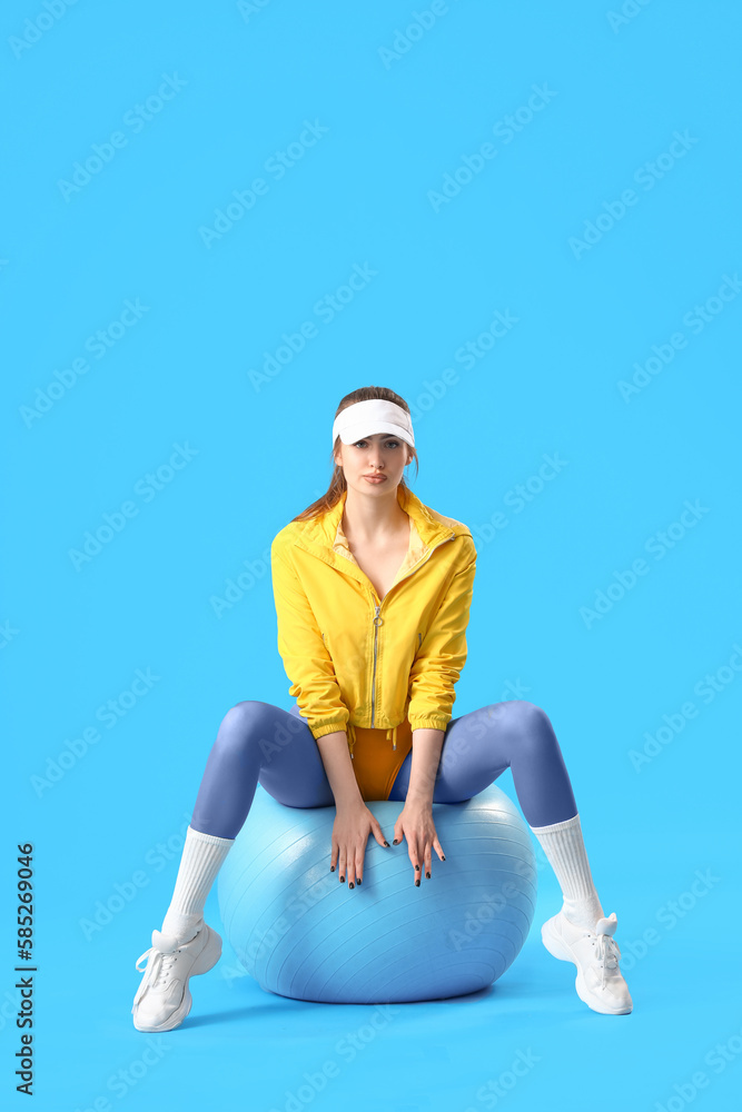 Sporty young woman with fitball on blue background