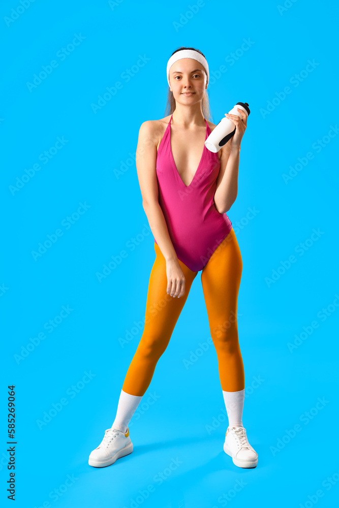 Sporty young woman with bottle of water on blue background