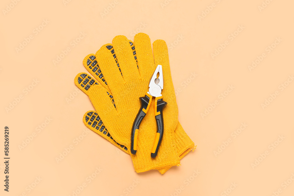 Pliers and gloves on beige background